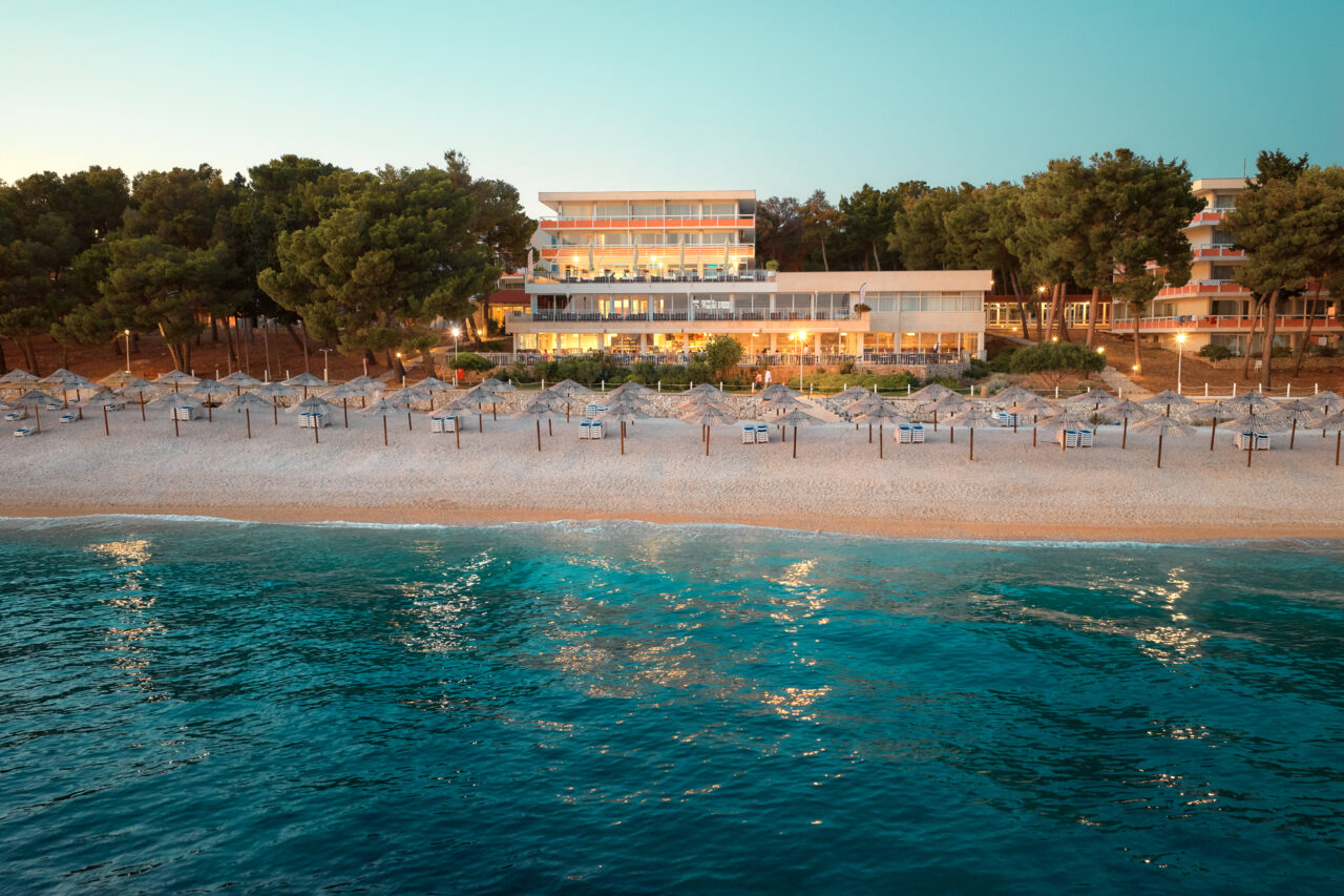Hotel Zora mit Restaurantterrasse und dem Strand bei Sonnenuntergang. 