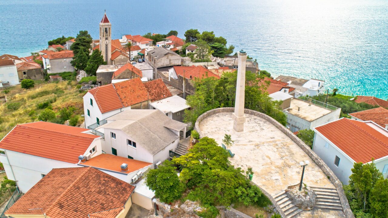 Gradac na Makarskoj rivijeri iz zraka, regija Dalmacija u Hrvatskoj, kuće, crkva i plato s spomenikom.