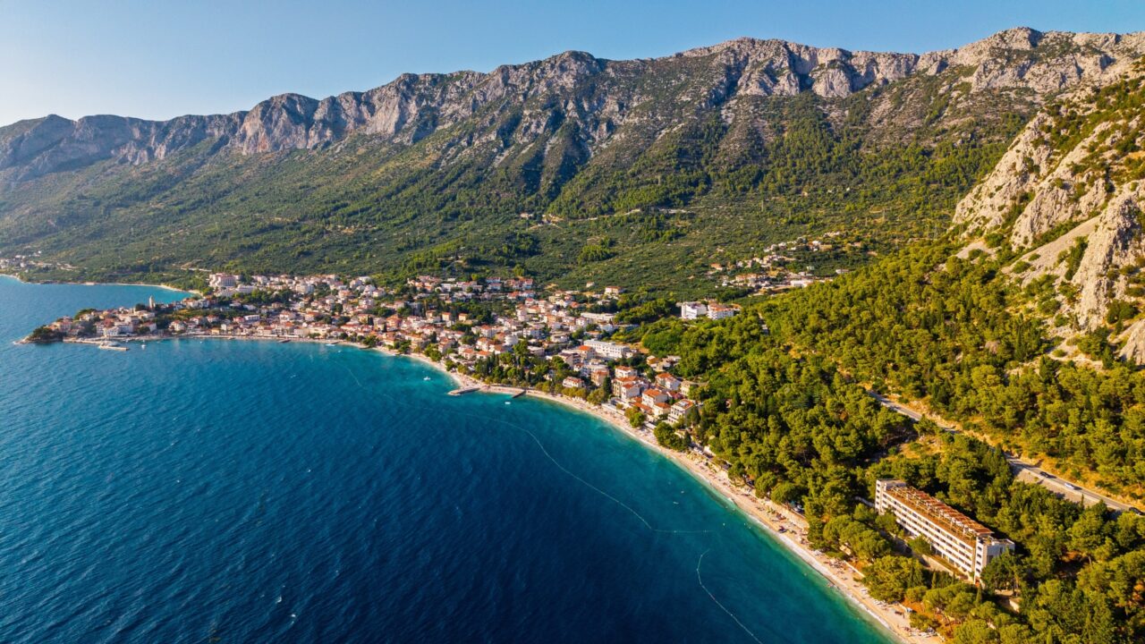 Zračni pogled na prekrasan primorski gradić Gradac na Makarskoj rivijeri u Hrvatskoj, s tirkiznim šljunčanim plažama Jadranskog mora i planinskim lancem Biokovo.